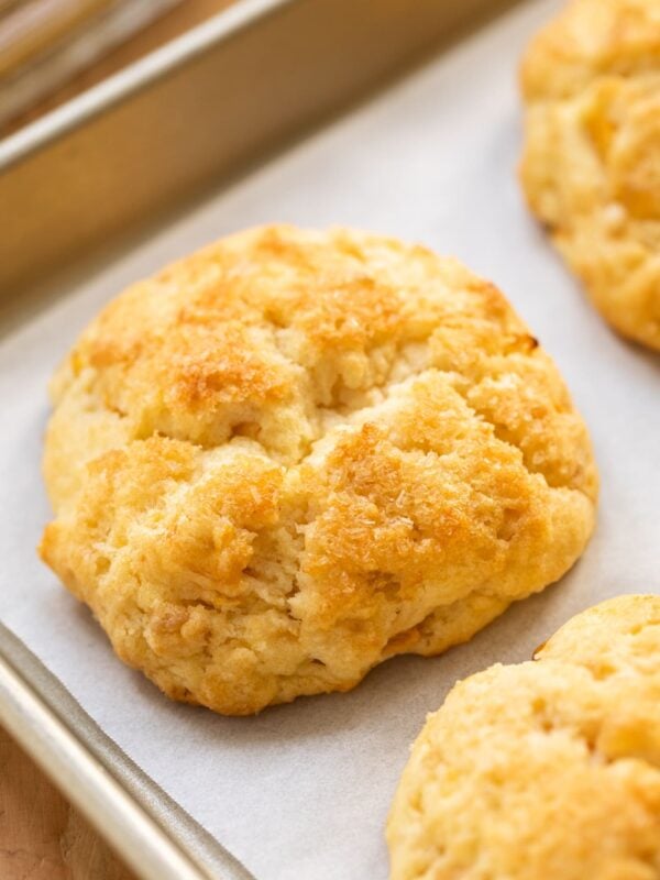 Golden brown biscuit sitting on piece of white parchment paper in a cooling rack all on wooden surface