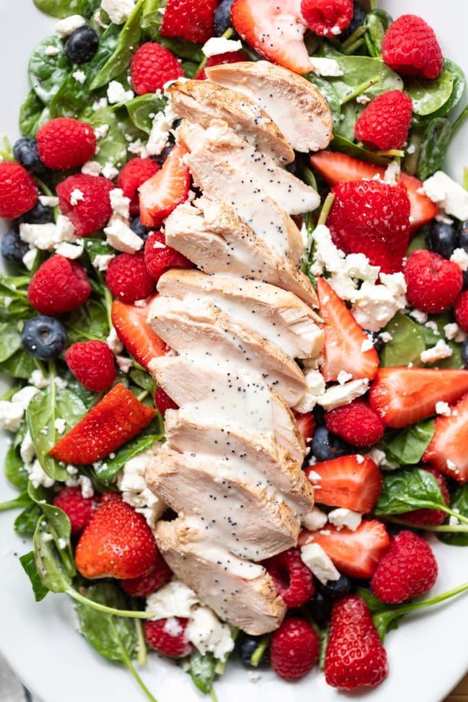 Pieces of grilled chicken layered on top of spinach with berries and drizzled with poppy seed dressing sitting on white plate