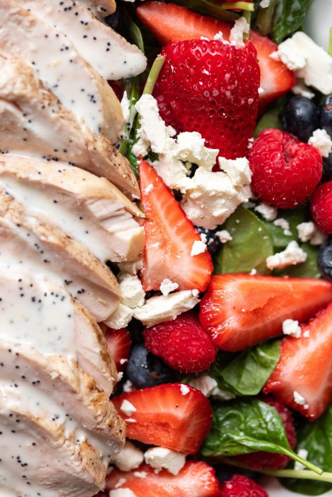 Pieces of strawberry and whole raspberries sitting on bed of spinach sprinkled with feta and layered with grilled chicken topped with lemon poppy seed dressing