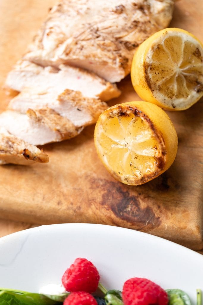Used lemons sitting on wood cutting board with sliced chicken