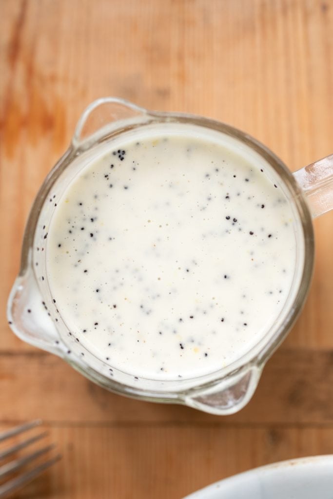 Top down view of lemon poppy seed dressing sitting in glass measuring cup on wood surface