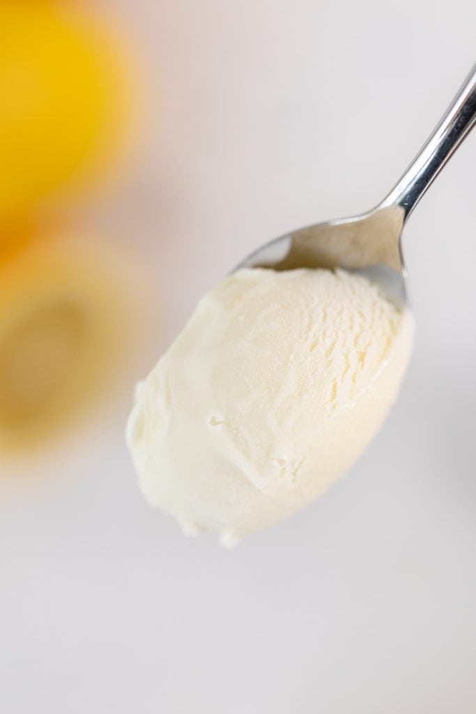 Spoon holding light yellow lemon thyme ice cream with corner of lemon in background
