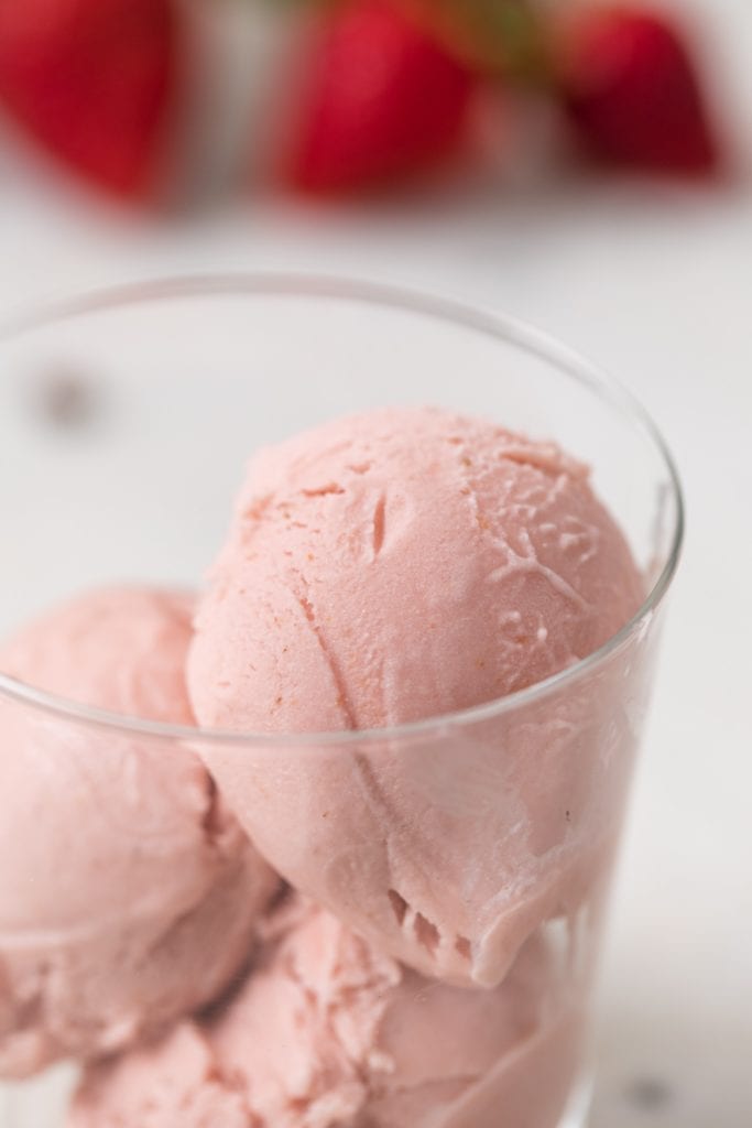 Close up view of strawberry basil ice cream in a clear glass cup with strawberries sitting on marble background