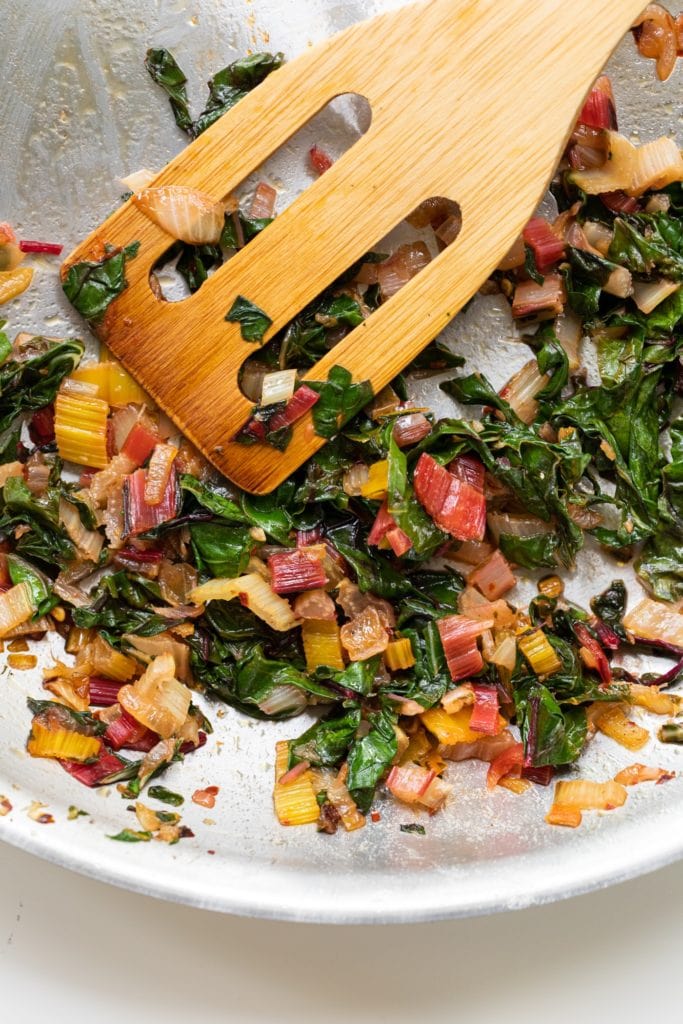 Wooden spatula sitting amongst Swiss chard mixture after being cooked on stove in stainless steel pan