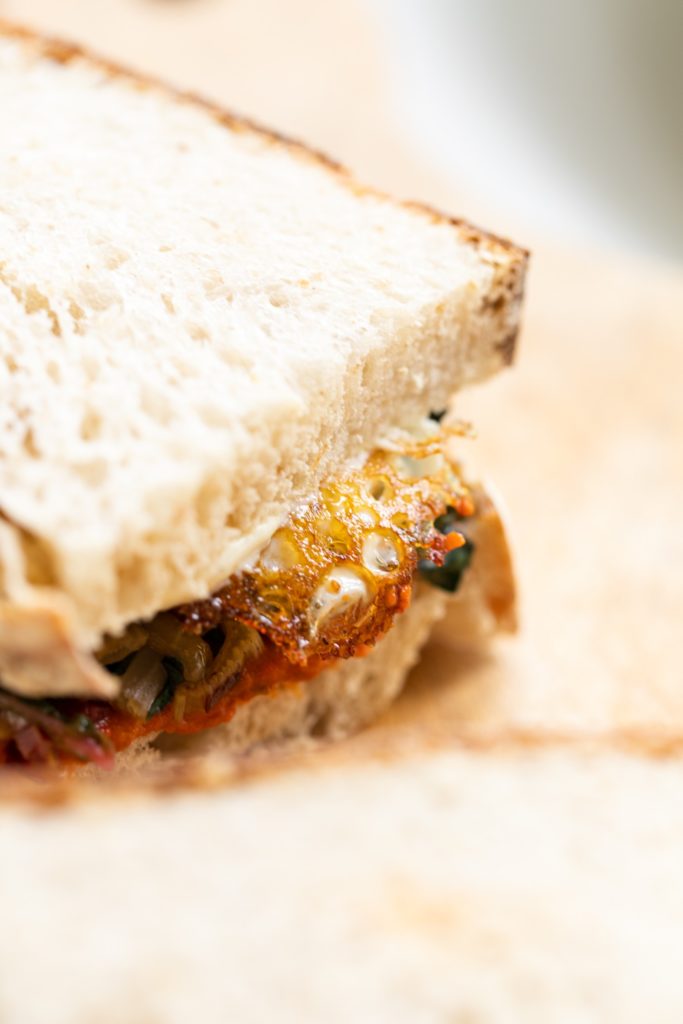 Close up view of sourdough bread with Swiss chard and harissa sauce on top of fried egg all on wood cutting board