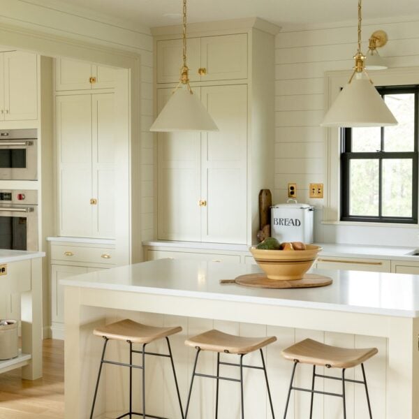 Kitchen stools sitting at a large island in a farmhouse kitchen with black windows and pantry cabinet in background