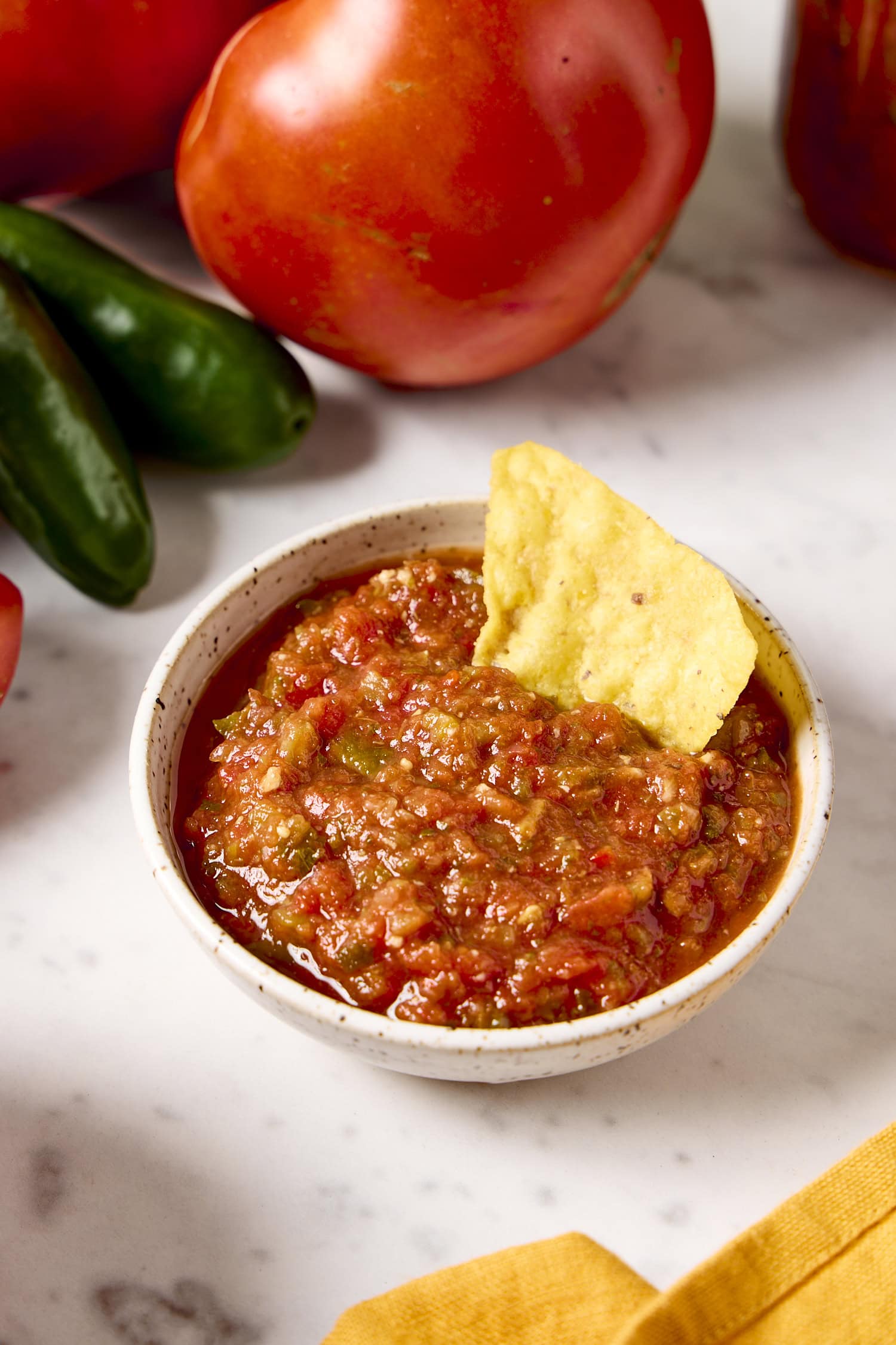 Small bowl filled with homemade salsa with a tortilla chip scooping up a portion.