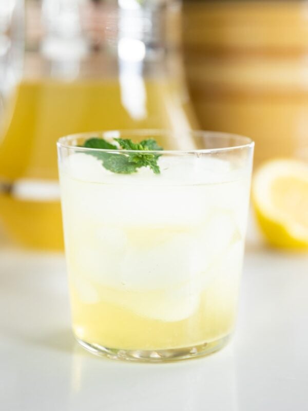 Small glass filled with yellow-colored garden mint tea with mint leaves on top all on white countertop