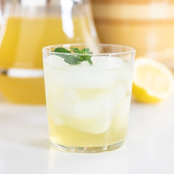 Glass filled with ice and yellow-colored garden mint tea with mint leaves as garnish on top all on white countertop