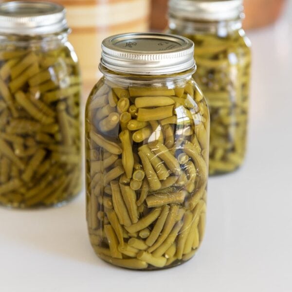 Three glass jars filled with sliced green beans sitting on white countertop with lids and rings on top