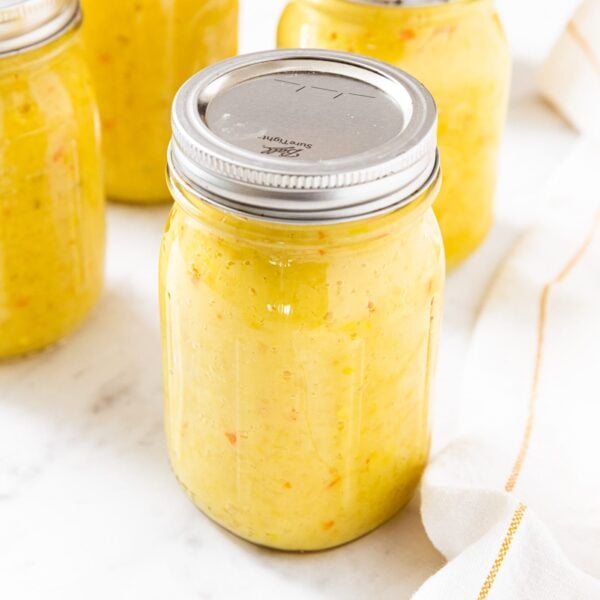 Glass jar filled with hot pepper mustard sitting on countertop with more glass jars all around.