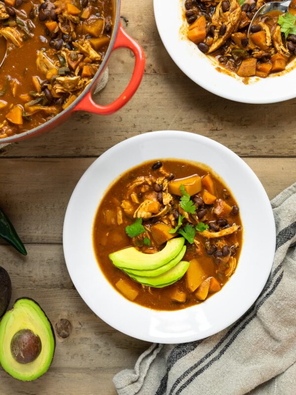 Top down view of white bowl of soup filled with red colored chili topped with slices of avocado
