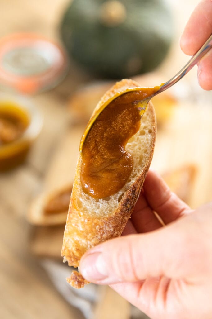 Spoon spreading pumpkin apple butter on top of piece of French bread with extra pieces of bread in background