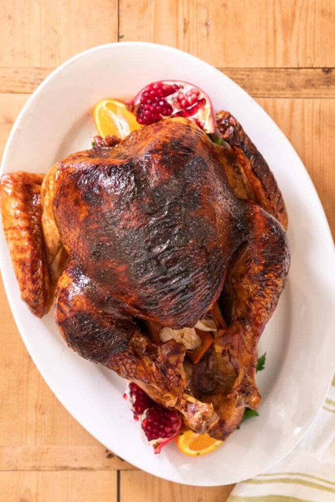 Top down view of a cooked turkey with browned skin sitting on a white platter with orange and pomegranate all on wood board