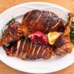 Top down view of brown-skinned pieces of turkey on white serving platter with pomegranate and slice of orange and parsley all on wood board