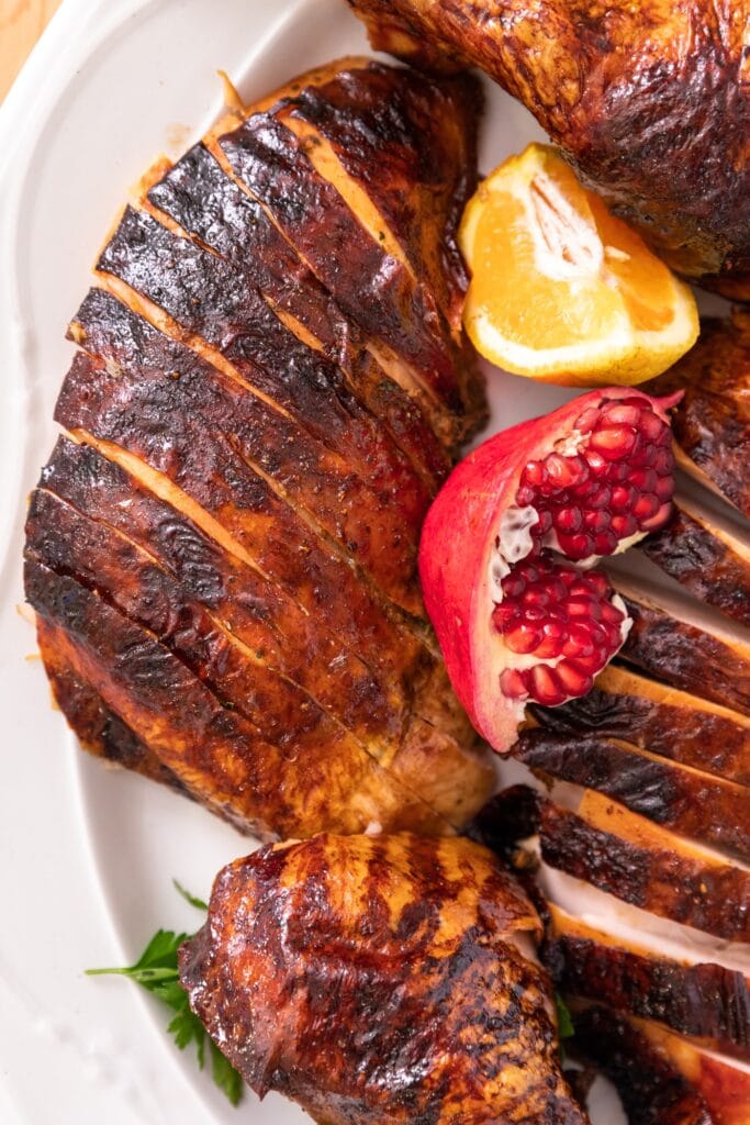 Top down view of crispy browned turkey skin sitting on white platter with open pomegranate and orange slice nestled among slices
