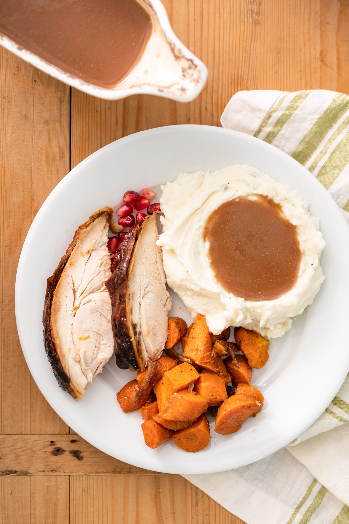 Top down view of plate filled with Thanksgiving dishes including white mashed potatoes topped with homemade gravy with extra gravy in white container to the side all on wood surface