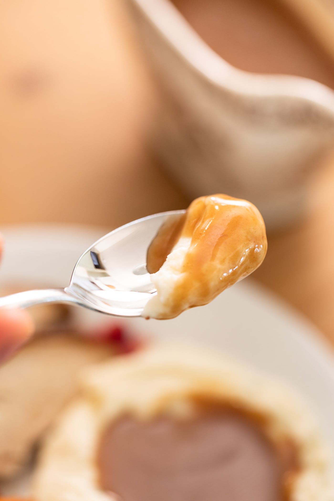 Spoon holding mashed potatoes covered in brown colored gravy with plate in background
