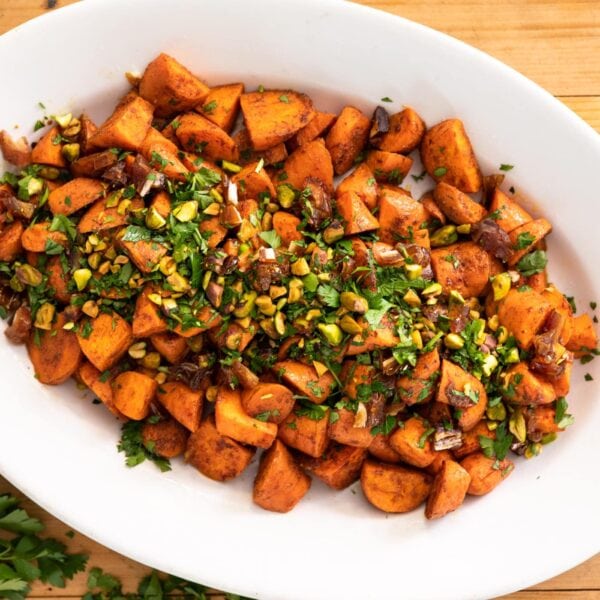 Top down view of orange carrots topped with green parsley sitting in white serving platter on wood surface with extra parsley