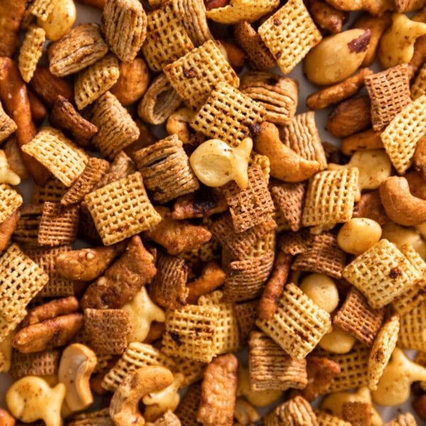 Top down view of browned pieces of cereal, pretzels, and nuts sitting on top of each other all on baking sheet after being toasted in the oven