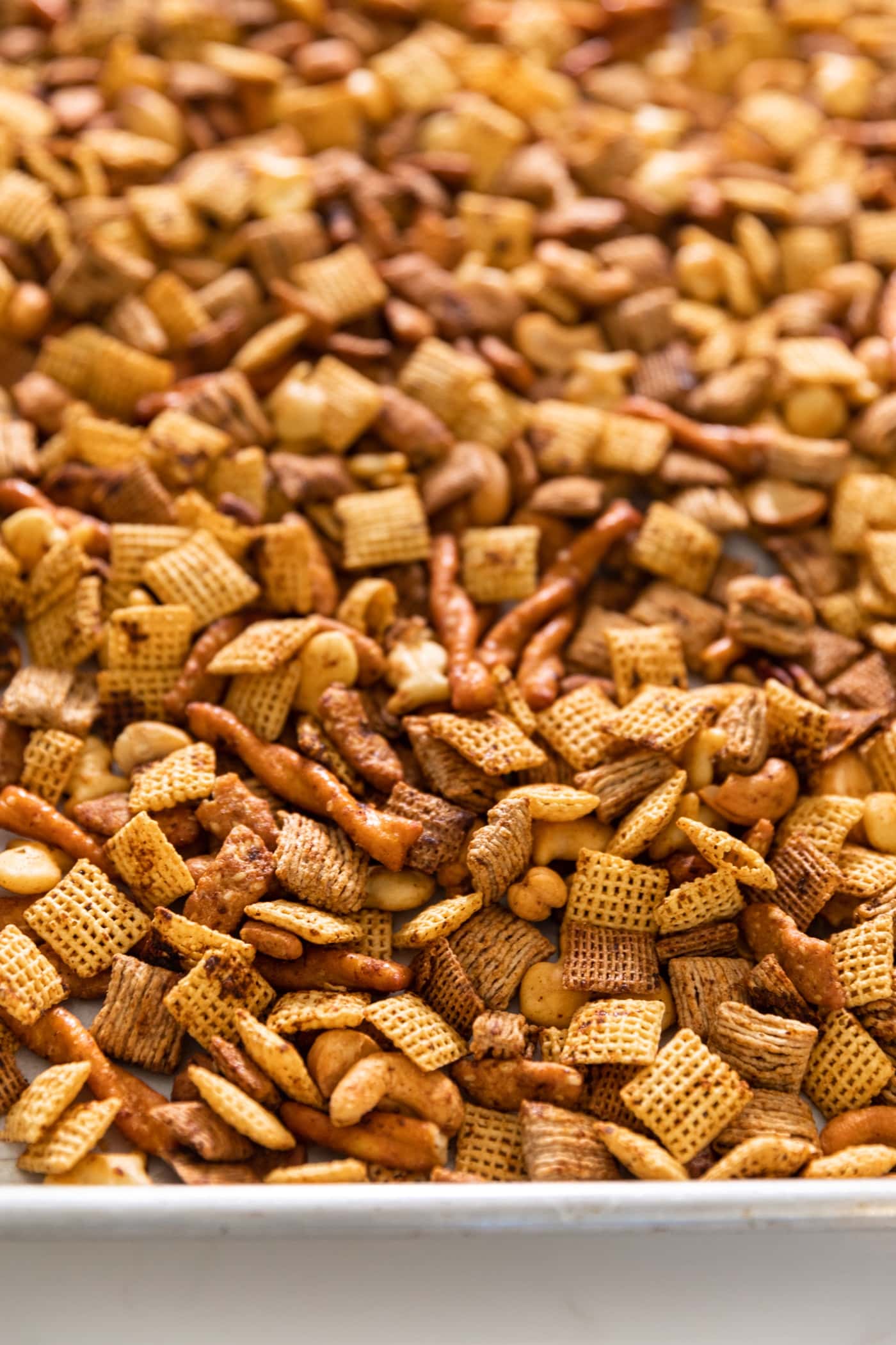 Baking pan sitting on white surface filled with cereal pieces and pretzels all toasted slightly in the oven