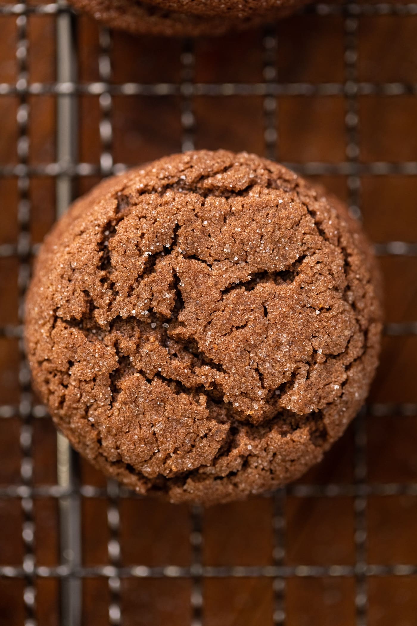 Top down close up view of top of chocolate cookie with cracks and sugar sprinkled on top sitting on wire cooling rack on wood surface