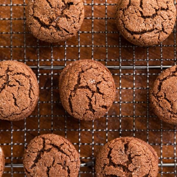 Top down view of brown colored cookies with cracks on the top sprinkled with white sugar and sitting on cooling rack on wood surface
