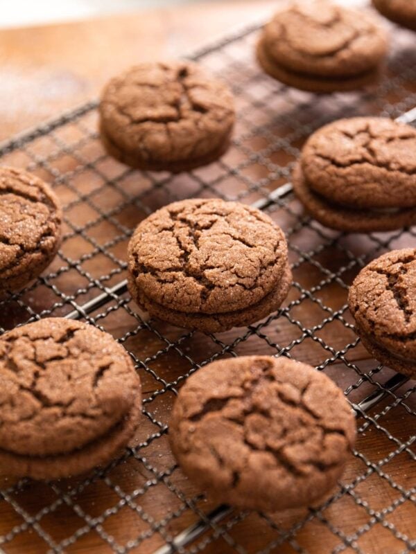 Side view of multiple chocolate thin mint sandwich cookies sitting on cooling rack all on wood surface