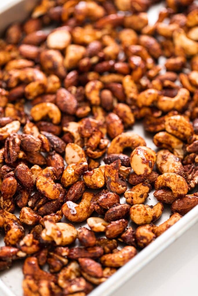 Spiced nuts sitting on silver baking pan after coming out of the oven on white countertop