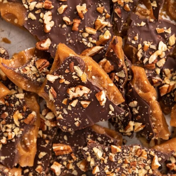 Top down view of broken pieces of English toffee piled on top of each other and sprinkled with chocolate and nuts