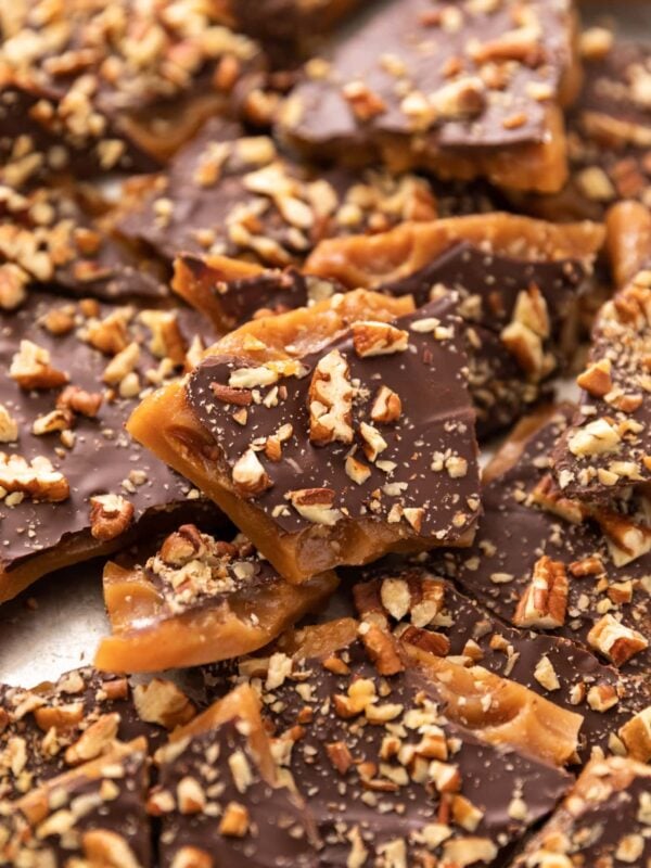 Pieces of toffee sitting in silver baking dish topped with pieces of nuts and chocolate