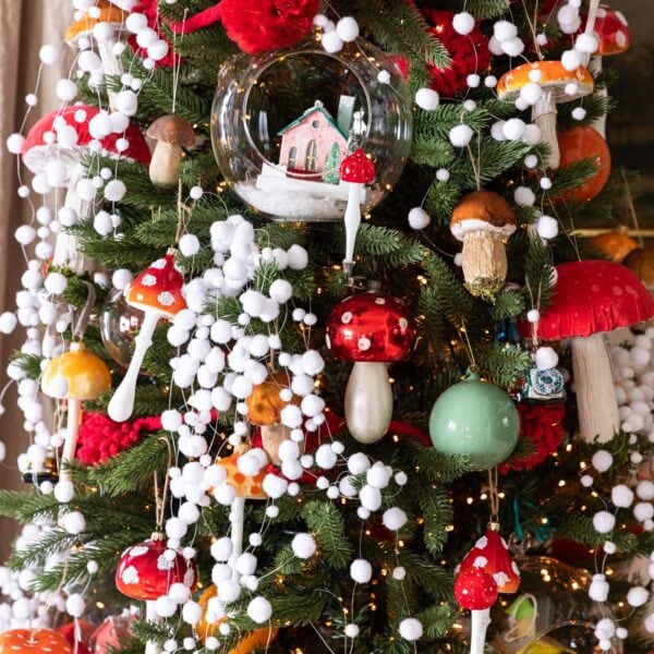 Red colored mushroom ornaments dangling from Christmas tree covered with white fake snow garland