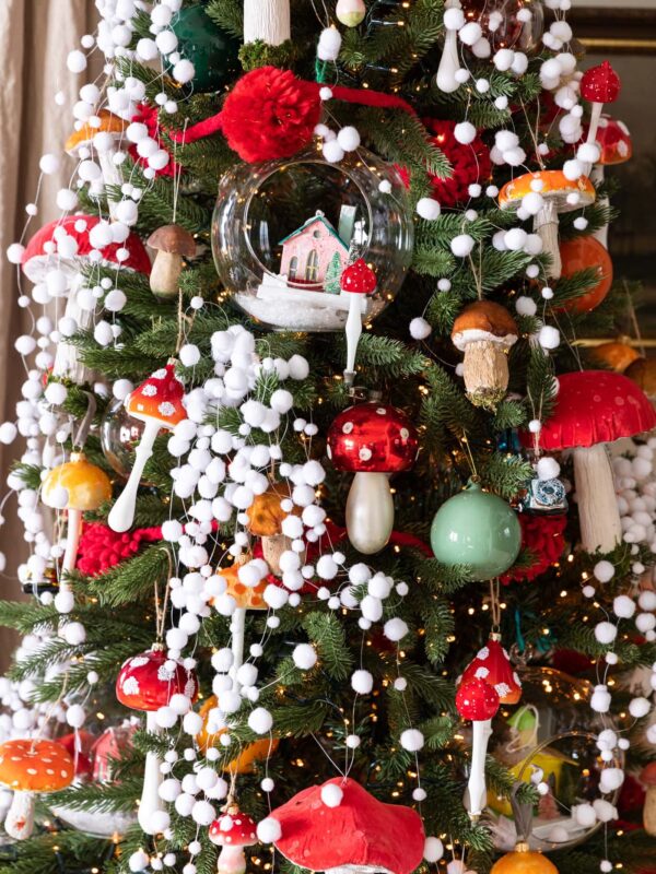 Red colored mushroom ornaments dangling from Christmas tree covered with white fake snow garland