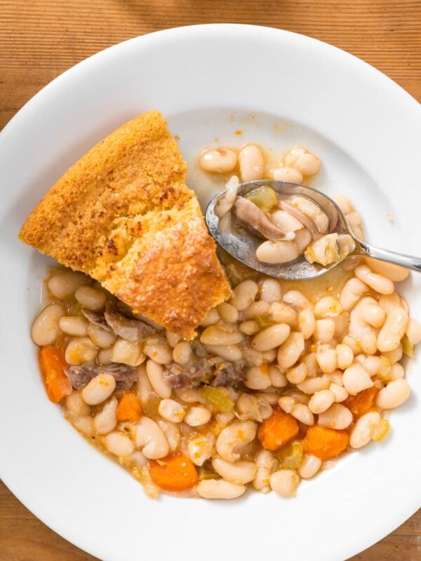Top down view of white bean and ham soup with slices of cornbread sitting amongst soup all on white bowl