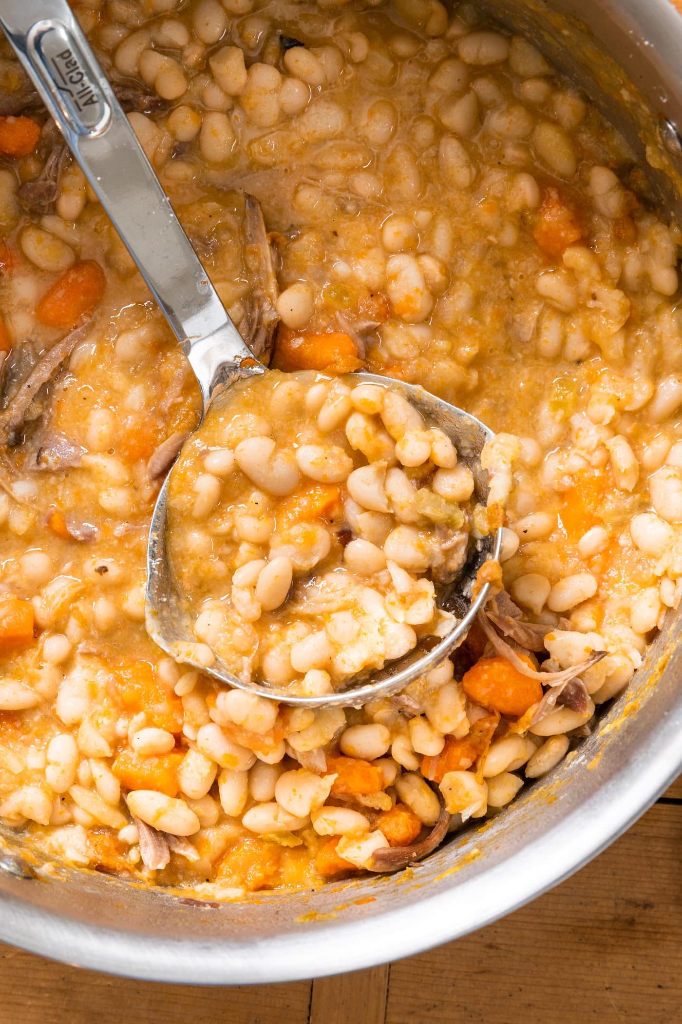 Top down view of yellow colored soup sitting in large silver kettle with ladle filled with soup