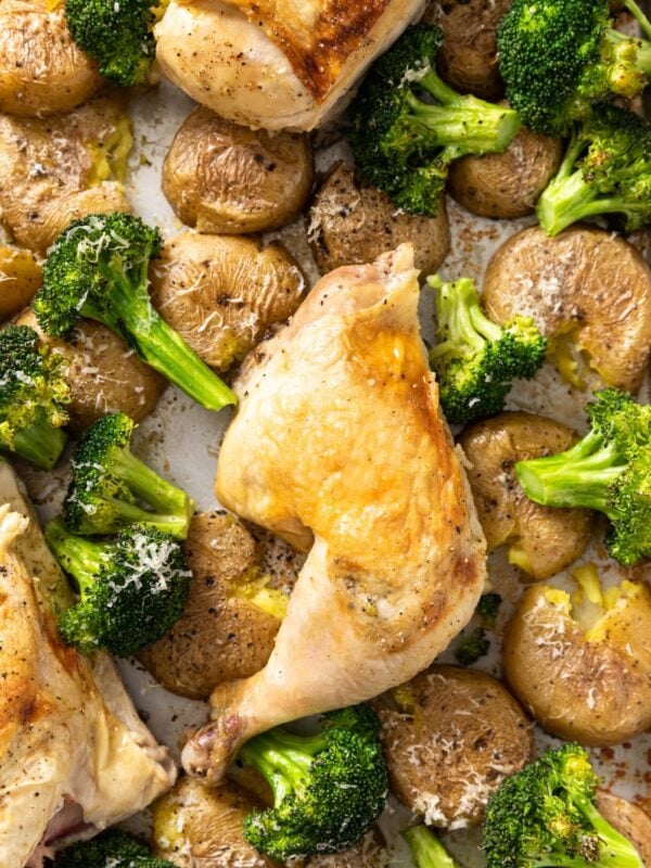 Top down view of roasted chicken breast on sheet pan nestled against broccoli and potatoes