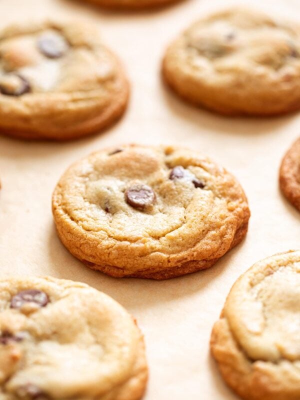 Multiple yellow colored chocolate chip cookies sitting on brown colored parchment paper.