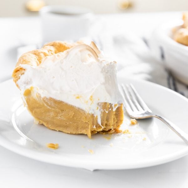 White plate with piece of brown colored butterscotch pie with creme brûlée topping with fork and rest of pie in background