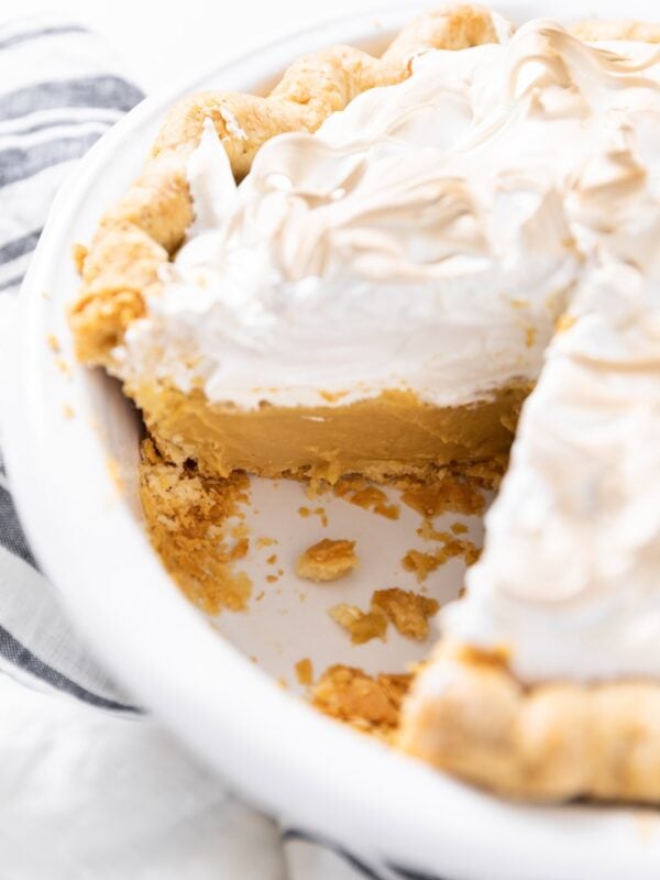 White pie plate filled with butterscotch pie with whipped cream topping browned on top.