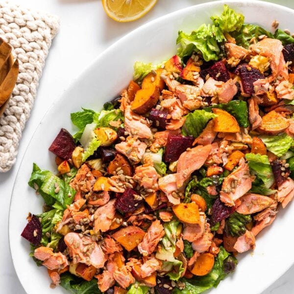 Top down view of salmon salad sitting on white platter with serving spoons sitting beside