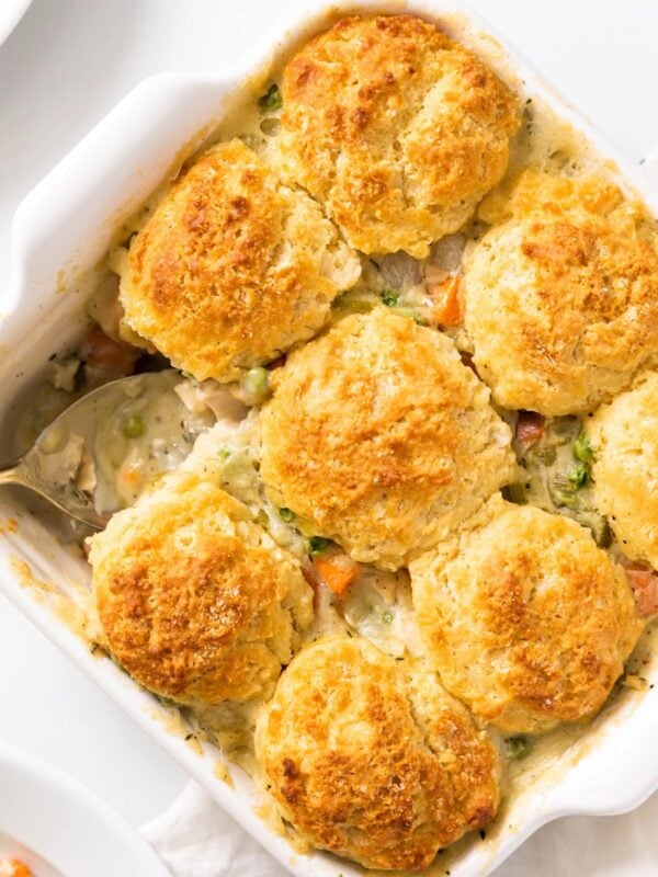 Top down view of yellow colored biscuits sitting in a white baking dish with spoon in corner all on white surface