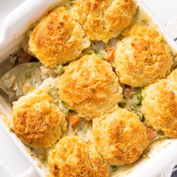 Top down view of yellow colored biscuits sitting on top of pot pie filling with spoon sitting in corner all on white surface