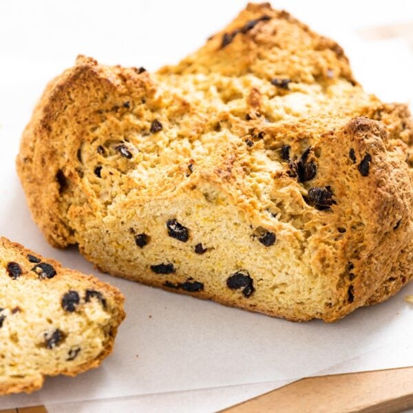 Circular brown colored loaf of bread with one side sliced off all sitting on white pieces of parchment on wood board