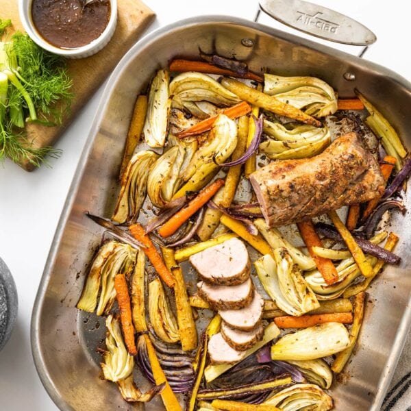 Top down view of white countertop with steel pan with sliced vegetables and roasted pork with slices cut off end