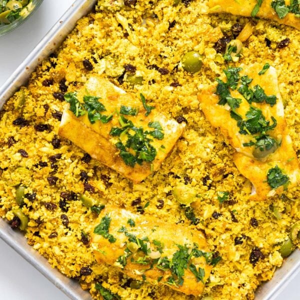 Top down view of sheet pan with yellow colored cauliflower rice with cod filets placed on top all on white surface