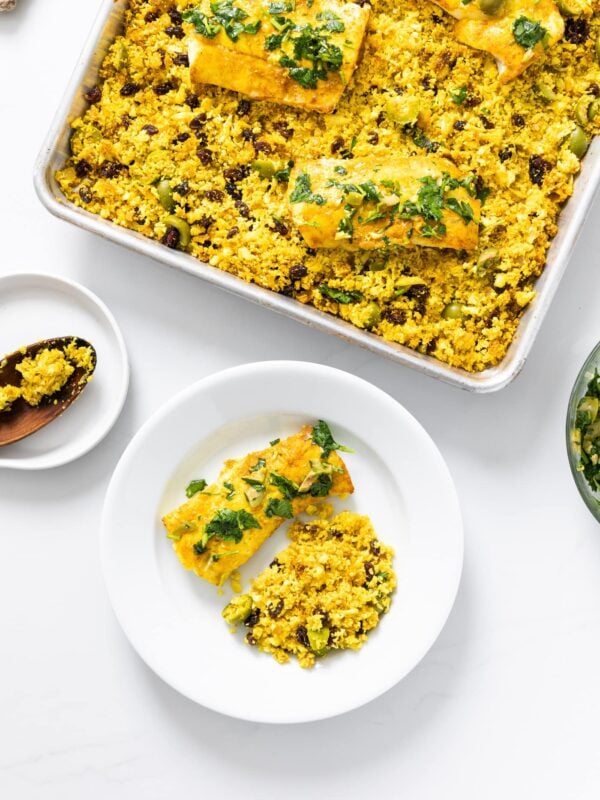 Top down view of white countertop with white plate and sheet pan containing yellow colored fish and cauliflower rice