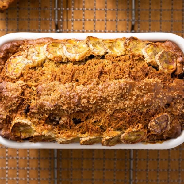 Top down view of decorated banana bread loaf sitting in white loaf pan resting on a cooling rack set on wood board