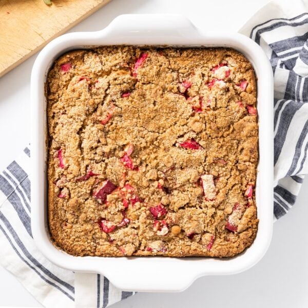 Top down view of coffee cake with pieces of rhubarb on top sitting in white baking dish all on white surface