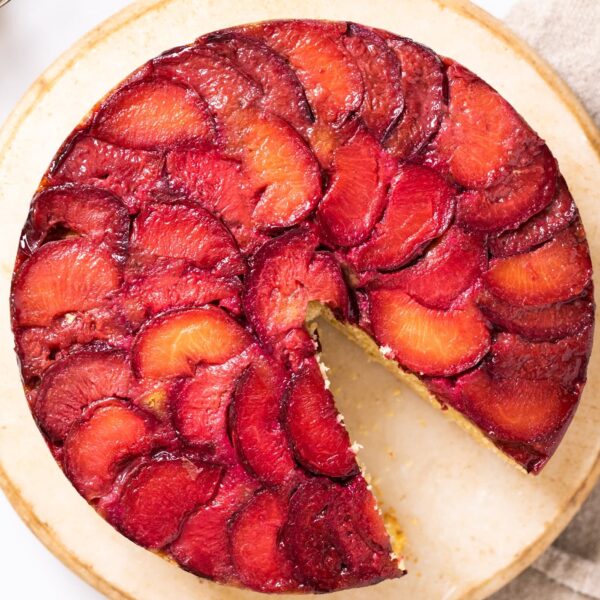 Top down view of plums laid out in an overlapping pattern on the top of a cake sitting on a cake stand with a towel underneath