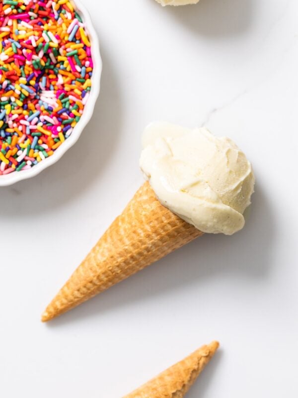 Top down view of vanilla ice cream in a cone with sprinkles in white container all on white countertop